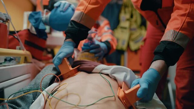 EMS Paramedics Team Provide Medical Help to Injured Patient on the Way to Hospital. Emergency Care Assistants Using a Defibrillator and Ventilation Mask to Bring the Man Back to Life in an Ambulance.