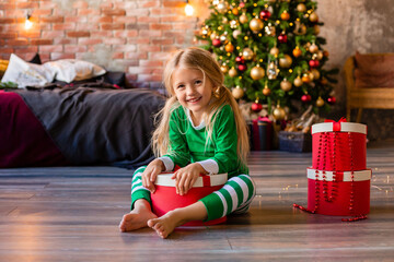cute little girl in pajamas near the Christmas tree pulls out of the gift box kitten. Christmas gifts, simple strstnto for text
