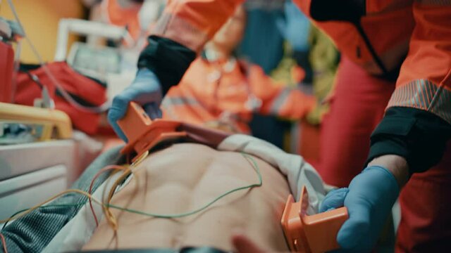EMS Paramedics Team Provide Medical Help to Injured Patient on the Way to Hospital. Emergency Care Assistants Using a Defibrillator and Ventilation Mask to Bring the Man Back to Life in an Ambulance.