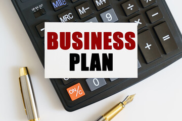 On the table there is a pen, a calculator and a business card on which the text is written - BUSINESS PLAN