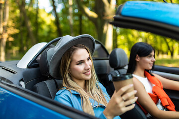 Fototapeta na wymiar Two young women friends drive convertible car in a road trip in summer