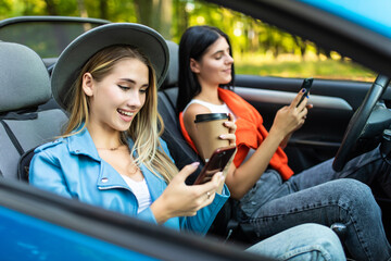 Fototapeta na wymiar Two women sit in car in front seats and use phones in convertible car