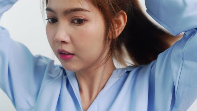 Young Asian woman doing long hair style looking in front mirror, Happy female make ponytail hairstyle to improve herself ready to working in bedroom at home. Lifestyle women at home concept.