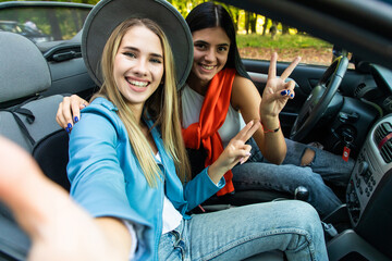 Two young beautiful women are doing a photo of yourself in a convertible car