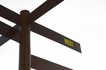 Dark coloured multidirectional signpost with applied direction to WEST text, isolated on white