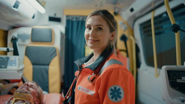 Calm and Happy Female EMS Professional Paramedic Smiles on Camera in Ambulance Vehicle. Successful Emergency Medical Technician on Their Way to a Call Outside the Healthcare Hospital.