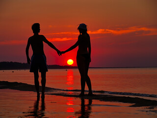 A couple in love holding hands on the beach at sunset 