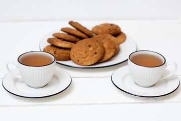 Two cups of tea and oatmeal cookies. Breakfast. Tea drinking. White wooden background.