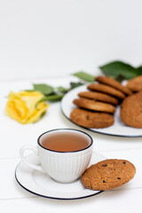A cup of tea and oatmeal cookies. Yellow rose. Breakfast. Tea drinking. White wooden background.
