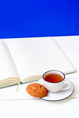 A cup of tea, a notebook and oatmeal cookies. Snack while studying. Education. Homework at school and university. Blue background
