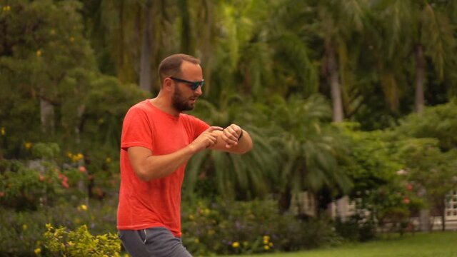 Man checking time on watch during jogging in city park, slow motion