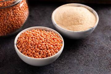 Red lentil and lentil flour in bowl on dark background.
