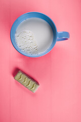 milk in blue cup and pieces of chocolate on a bright pink background. healthy lifestyle concept