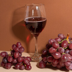 Close-up view of wineglass with red wine and bunch of grapes on beige background. The shadow on the wall. Wine is always good idea. Tasty alcohol.