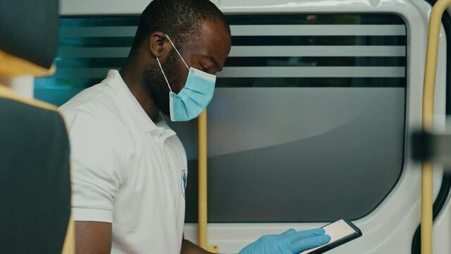 Black African American Paramedic in Face Mask Using Tablet Computer while Riding in Ambulance Vehicle for an Emergency. Emergency Medical Technicians Outside the Healthcare Hospital. Covid-19 Concept.