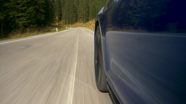 CLOSE UP Brand new blue car speeds down scenic switchback road running through the idyllic woods in Tre Cime. Sports car navigates a challenging serpentine route leading through the woods in Dolomites