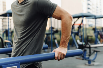 Close up shot of muscle of young man doing dips on uneven bars outdoors. Introduction to sports and a healthy lifestyle