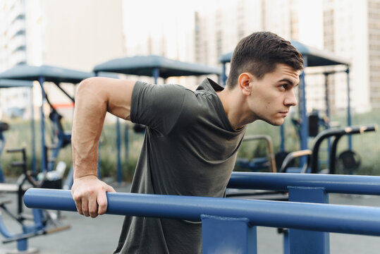 Handsome Young Man Doing Dips On The Uneven Bars On The Outdoor Sports Field. Healthy Lifestyle, Sports And Endurance Concept