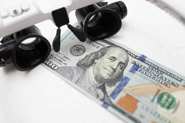 checking a hundred dollar bill with a magnifying glass, glasses with a microscope. How to identify...