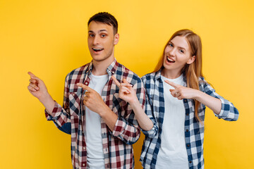 Happy beautiful young couple, man and woman, pointing with fingers at copy space isolated on yellow background