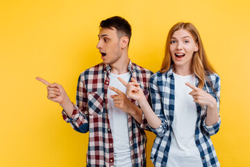 Happy beautiful young couple, man and woman, pointing with fingers at copy space isolated on yellow background