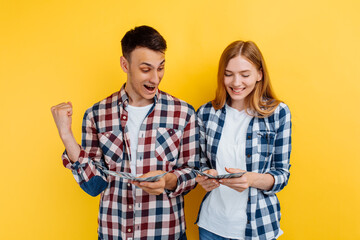 Excited couple, man and woman, holding dollar bills and celebrating isolated on yellow background