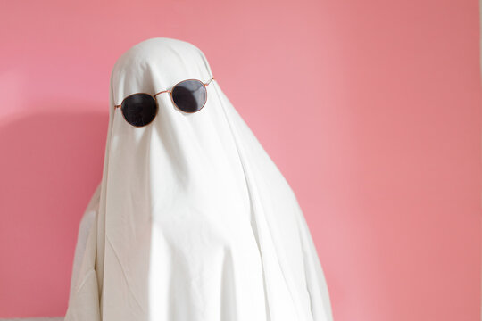 Cute sheet ghost costume with sunglasses on a pink background. Halloween party carnival concept.