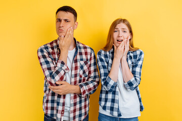 Young couple, man and woman suffering from toothache, holding on to the cheek, on yellow background