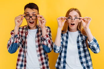 young excited people, man and woman wearing glasses for vision on yellow background