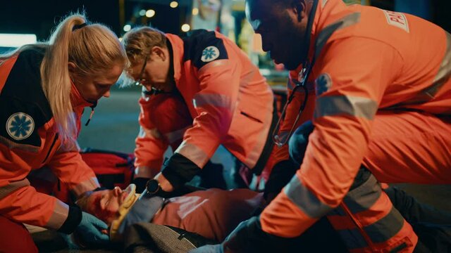 Team of EMS Paramedics Provide Help to an Injured Young Man. Doctor in Gloves Attaches Cervical Neck Collar on a Patient. Emergency Care Assistants Arrived in an Ambulance Vehicle at Night.