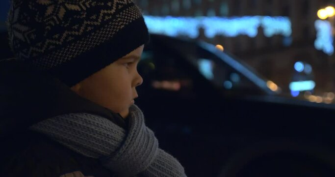 Child Stands on Street Watching Police Flashing Lights Busy City Traffic at Night Downtown Street. Blurred Background