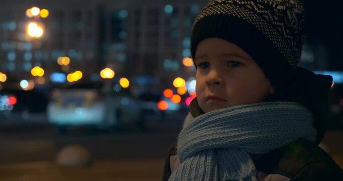 Child Stands on Street Watching Police Flashing Lights Busy City Traffic at Night Downtown Street. Blurred Background