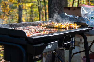 Bacon and potatoes cooking on an outdoor griddle