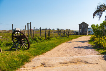 Obraz premium old road and wooden house in the distance with wheels on the side and wire fence