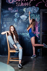 Fototapeta na wymiar back to school after summer vacations, two teen real girls in classroom with blackboard painted together, lifestyle people concept
