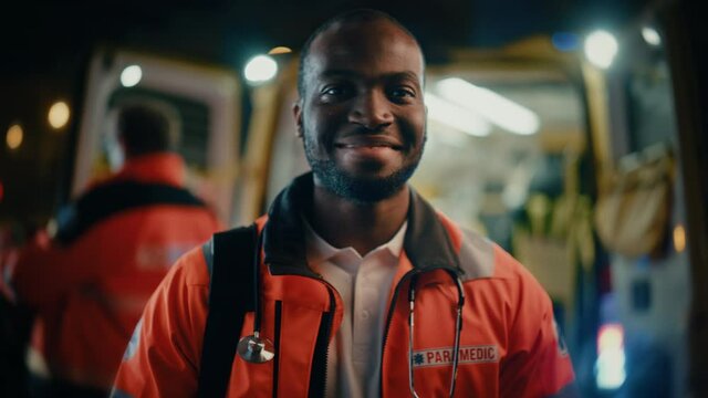 Portrait of a Black African American EMS Paramedic Proudly Standing in Front of Camera in High Visibility Medical Orange Uniform and Smiling. Successful Emergency Medical Technician or Doctor at Work.