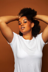 pretty young african american woman with curly hair posing cheerful gesturing on brown background, lifestyle people concept