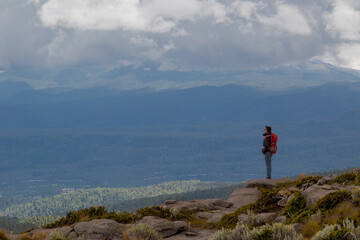 Male hiker with a backpack standing on the edge of a cliff with a beautiful nature scene behind
