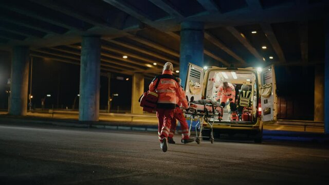 Team of EMS Paramedics React Quick to Provide Medical Help to Injured Patient and Get Him in Ambulance on a Stretcher. Emergency Care Assistants Arrived on the Scene of a Traffic Accident on a Street.