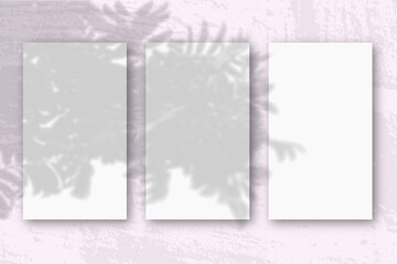 3 vertical sheets of textured white paper on soft pink table background. Mockup overlay with the plant shadows. Natural light casts shadows from an exotic plant. Horizontal orientation