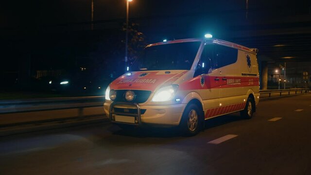 Parallel Moving Footage of an Ambulance Vehicle with Working Strobe Light and Signal Driving to Emergency Call on a City Urban Street at Night