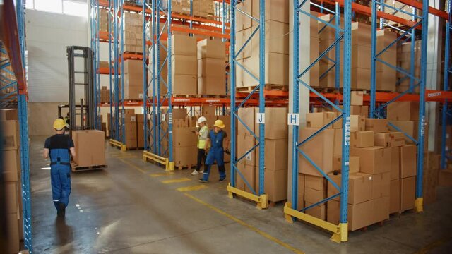 Retail Warehouse full of Shelves with Goods in Cardboard Boxes, Male and Female Supervisors Use Digital Tablet Discuss Product Delivery while Scanning Packages.Forklift Working in Logistics Storehouse