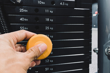 Young athlete hand change weight on iron heavy plates stacked of weight machine in gym and fitness...