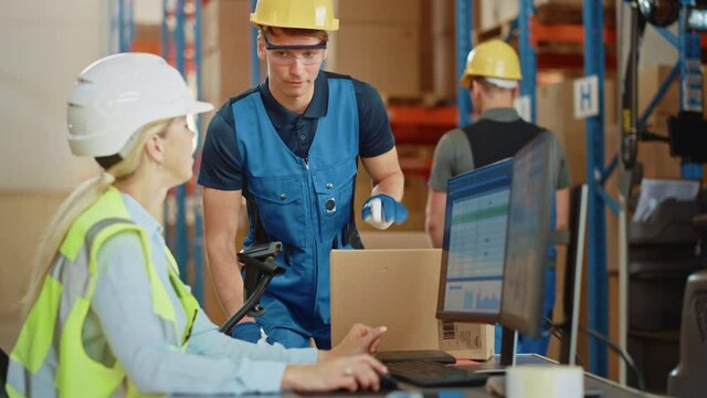 In Retail Warehouse Manager Uses Computer with Inventory Checking Software, Talks with Storehouse Worker about Package Delivery