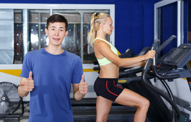 Fototapeta premium Young sporty man coach posing in gym with fitness machines on background