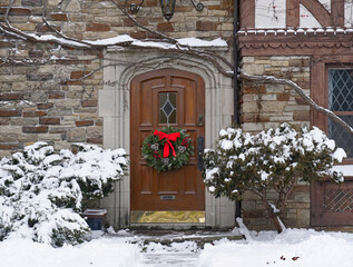 Wooden front door with Christmas wreath of house with snow covered evergreen shrubs
