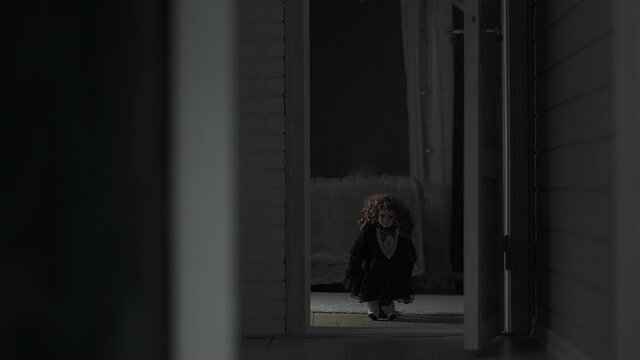 Small creepy girl doll standing in the middle of a door frame, staring at the camera.