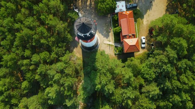Aerial close-up view of Stilo Lighthouse and green forest around it - lighthouse located in Osetnik (formerly Stilo) on the Polish coast of the Baltic Sea, close to the village of Sasino, flying up