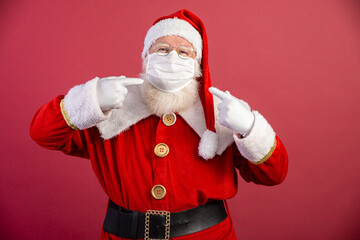 Real Santa Claus with a red background, wearing a protective mask, glasses and hat. Christmas with social distance. Covid-19