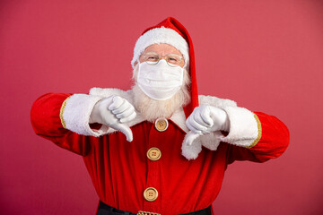 Fototapeta na wymiar Real Santa Claus with red background, wearing protective mask, glasses and gloves with thumbs down. Christmas with social distance. Covid-19